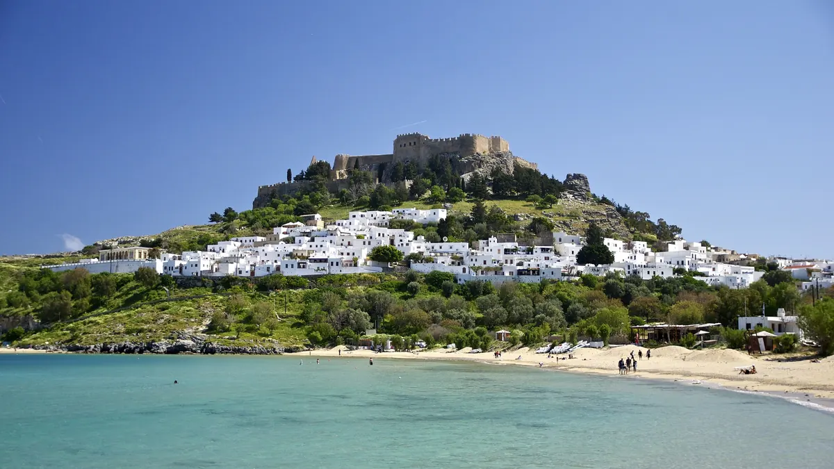Satul Lindos din Rodos: case albe pe deal, cetatea cu acropola în vârf și plaja cu apă turcoaz din golf