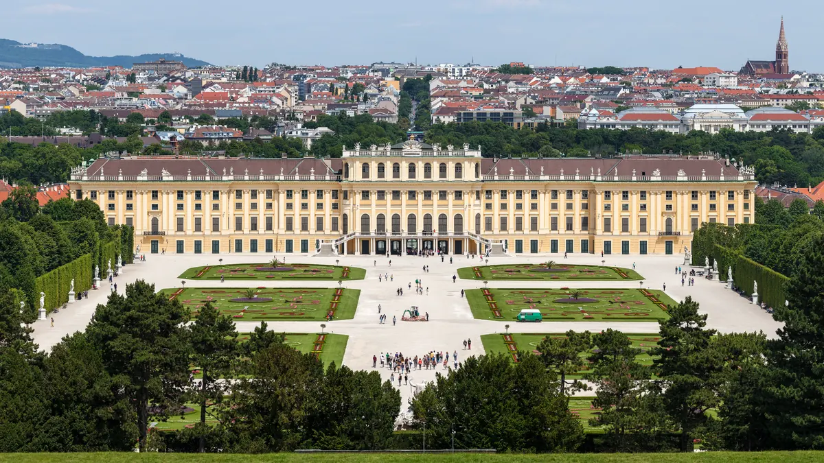 Palatul Schönbrunn din Viena văzut de pe dealul Gloriette: fațada galbenă, grădinile cu straturi de flori, parcul și acoperișurile orașului în fundal